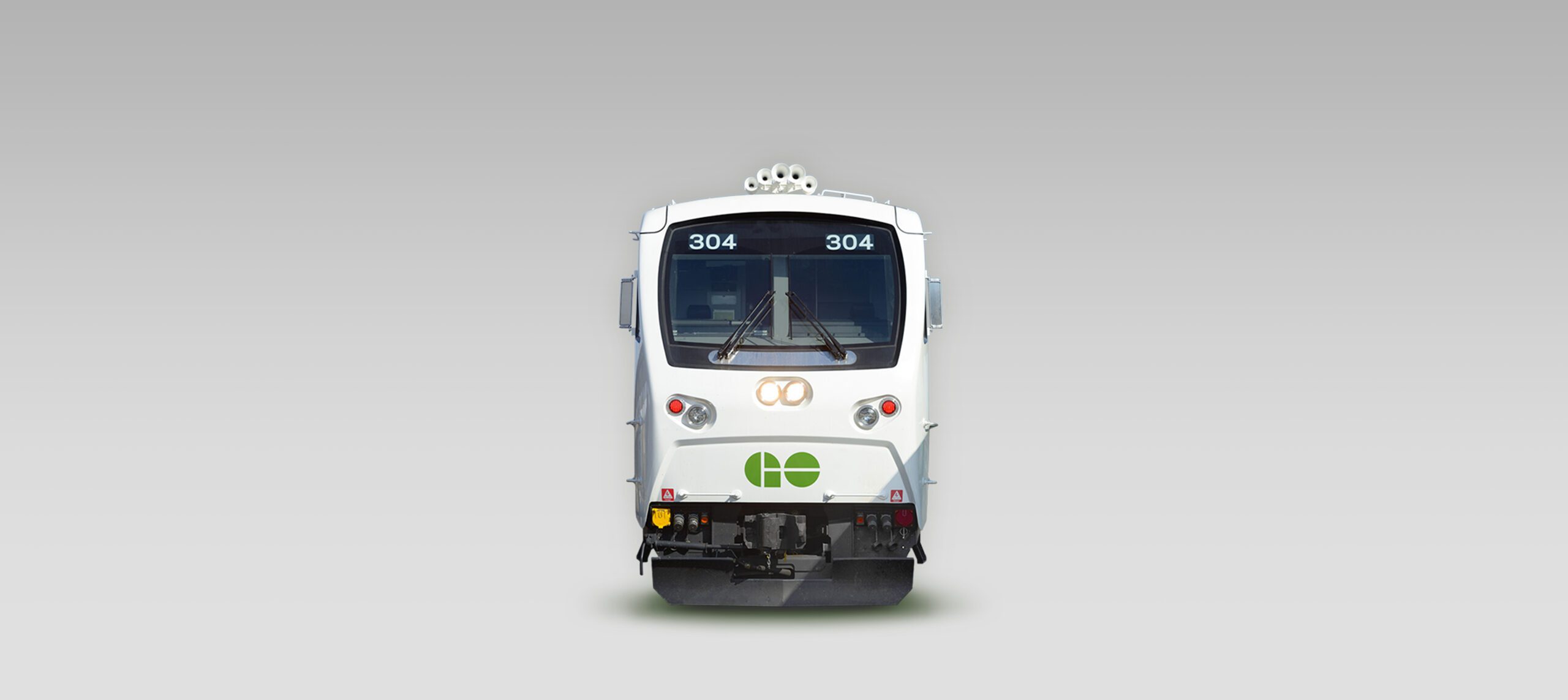 A white commuter train viewed from the front, displaying the numbers 304 and featuring a green GO Transit logo on a plain grey background, showcases the expertise of an Agence d'ingénierie mécanique à Montréal.