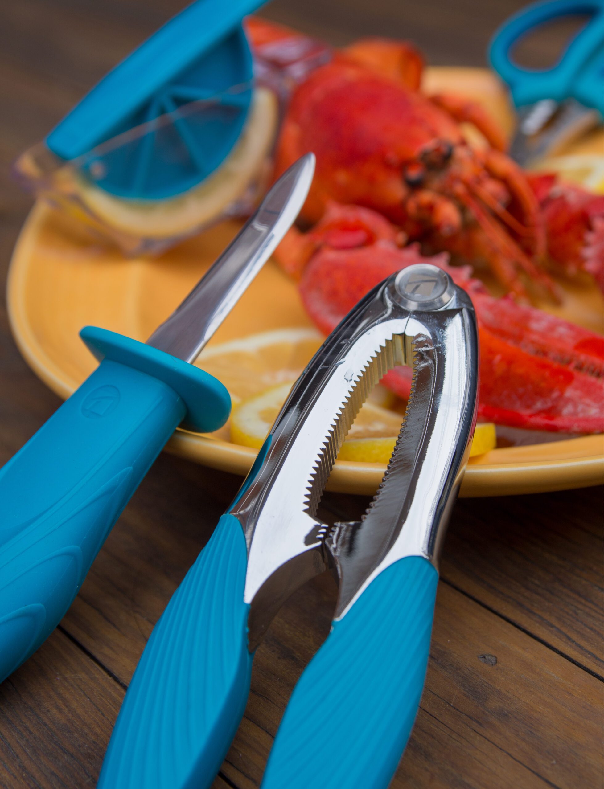 A close-up of blue-handled seafood tools, including a lobster cracker and knife, on a wooden table next to lobster and lemon slices—showcasing refined design reminiscent of une stratégie de design au Québec.