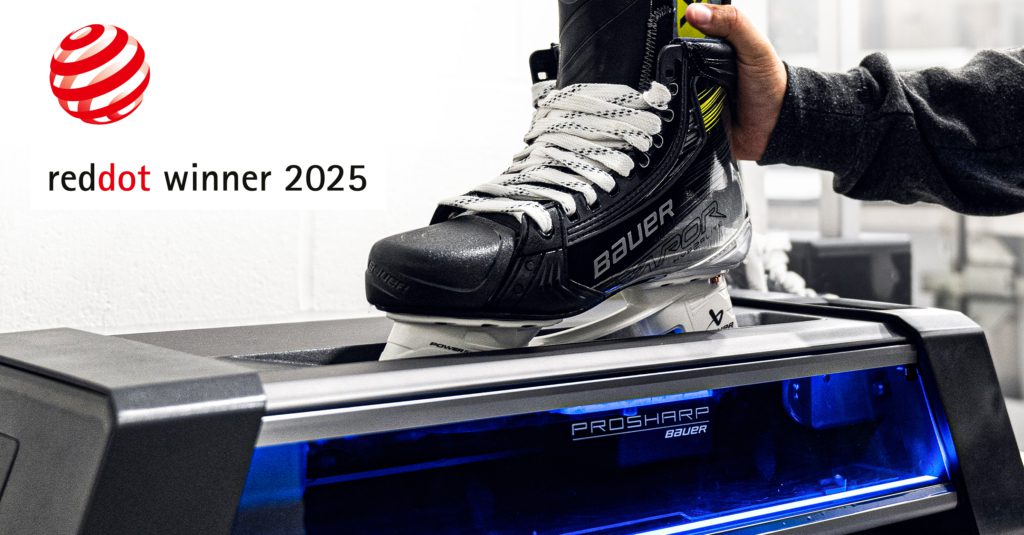 Une personne place un patin de hockey Bauer sur une machine ProSharp, mettant en valeur l'expertise d'une agence de design industriel à Montréal. Le logo du lauréat du prix Red Dot 2025 apparaît dans le coin supérieur gauche.