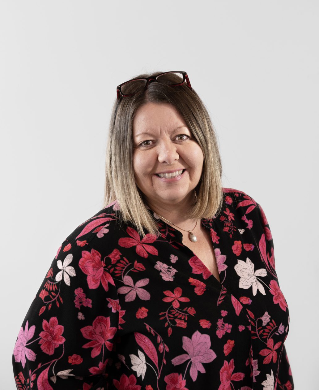 Une femme aux cheveux lisses jusqu'aux épaules, portant des lunettes sur la tête et un chemisier noir à motifs floraux roses et rouges, sourit à la caméra - un look professionnel pour une Agence de développement de produits à Montréal.