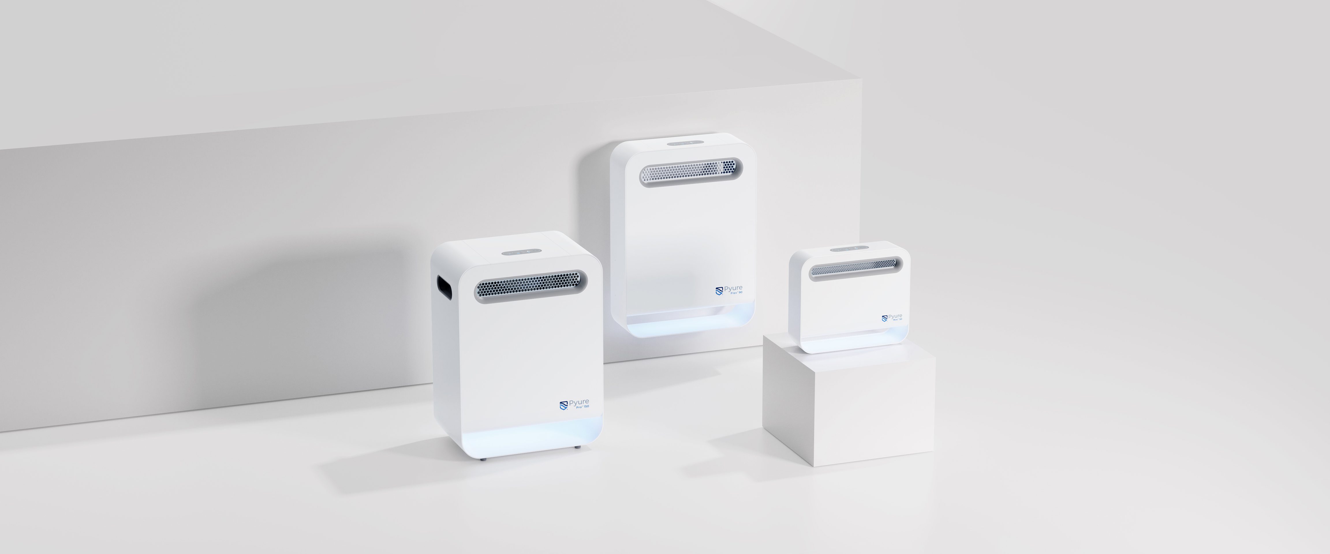 Trois purificateurs d'air blancs, rectangulaires et de tailles différentes sont présentés sur des plates-formes blanches sur un fond gris clair minimaliste - mettant en valeur l'élégante Stratégie de design au Québec avec des évents sur le devant et un petit logo près du bas.